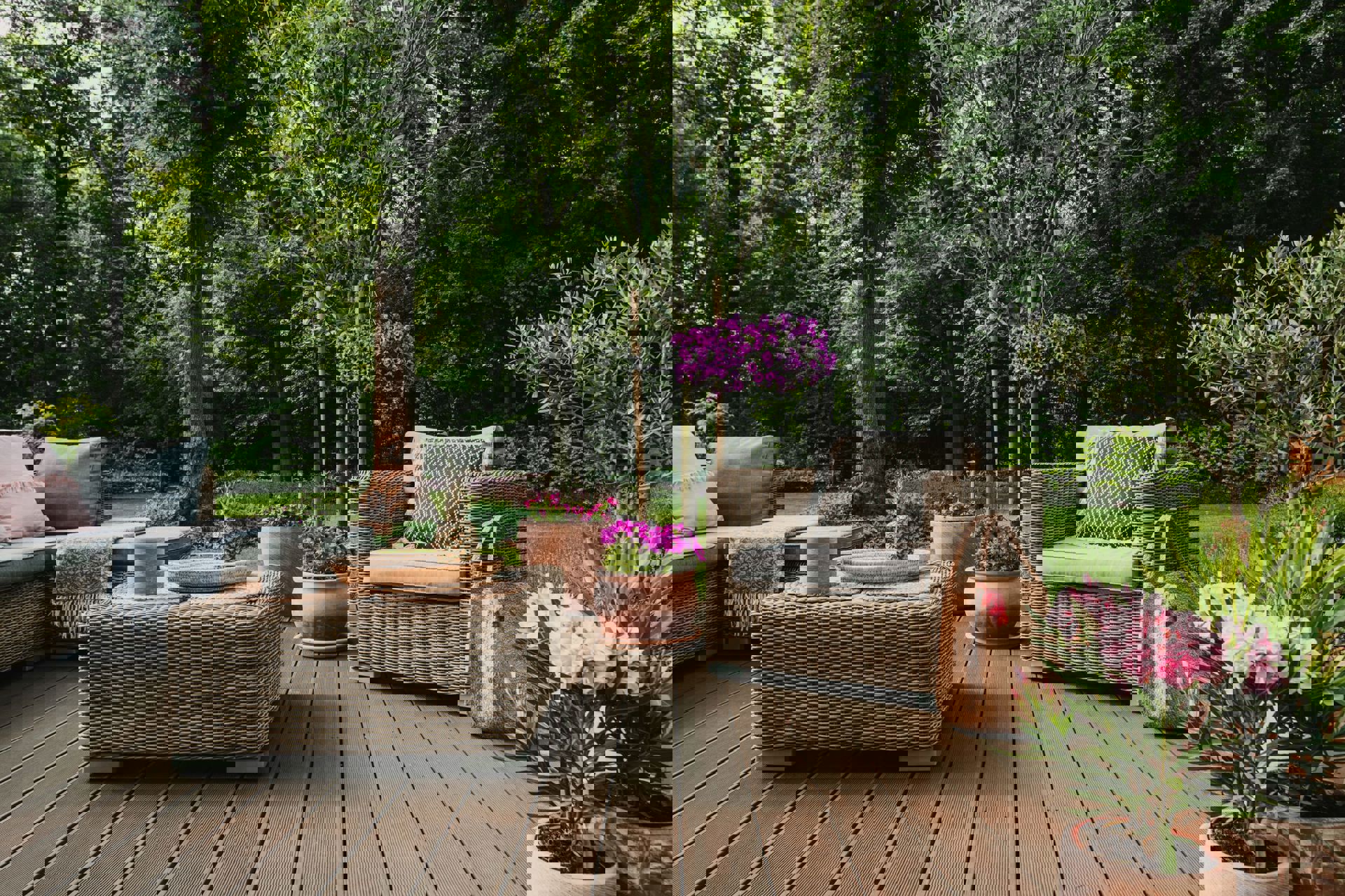 A deck is staged with outdoor patio furniture and planters full of flowers.