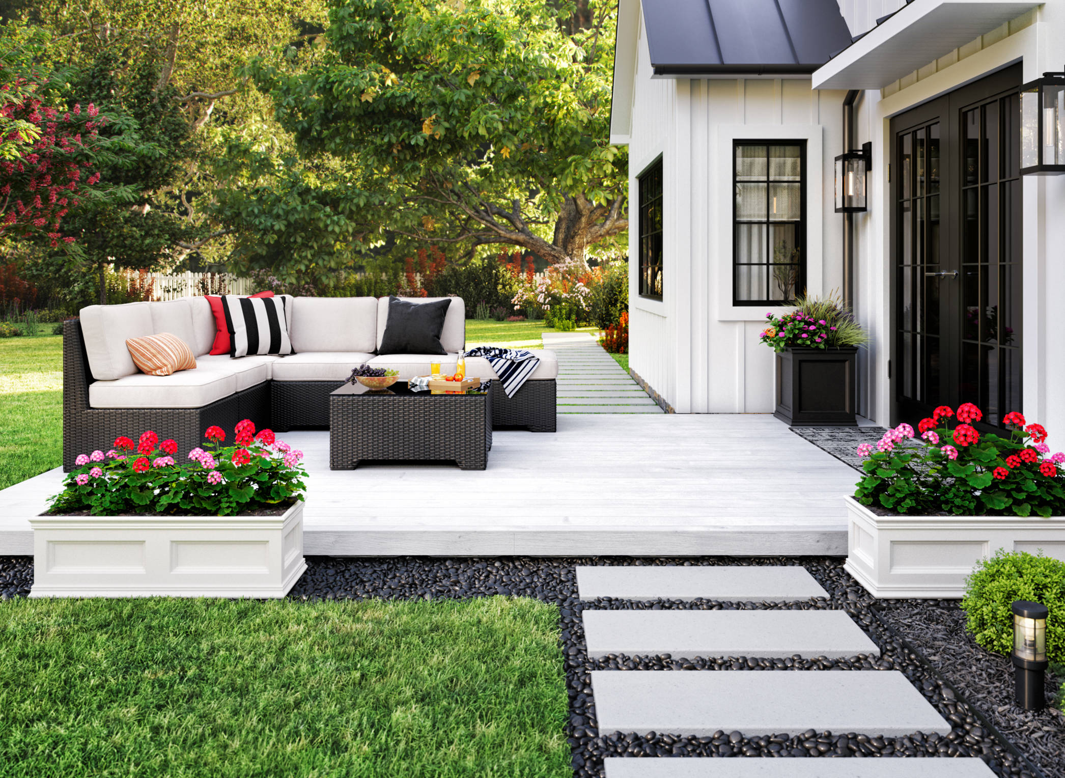The image above shows an outdoor patio attached to a white house. The white deck holds a sofa and table. It sits atop gravel surrounded by grass.