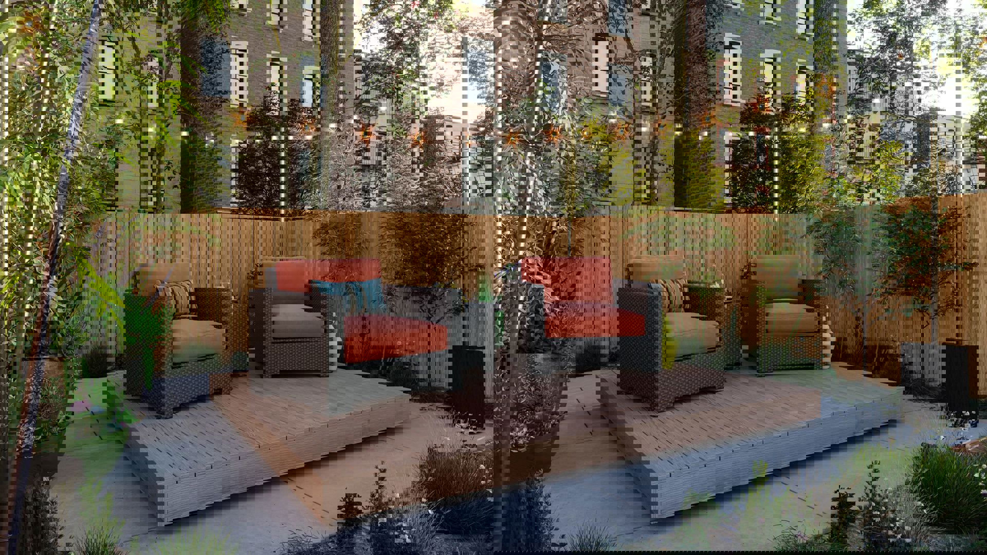 This image depicts a deck with two chairs and a small table on it. Trees and plants are placed along the fence of this outdoor space.